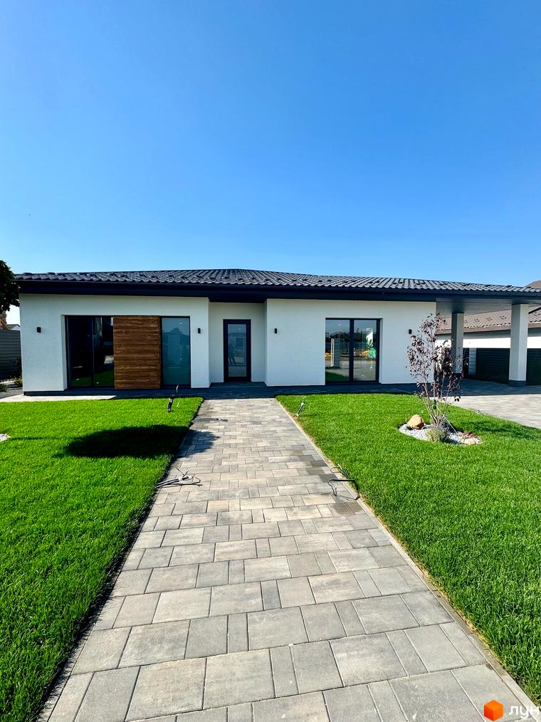 Вигляд будинку в Котеджному містечку Bratske Home з доріжкою та зеленим газоном. На задньому плані видно чисте блакитне небо.