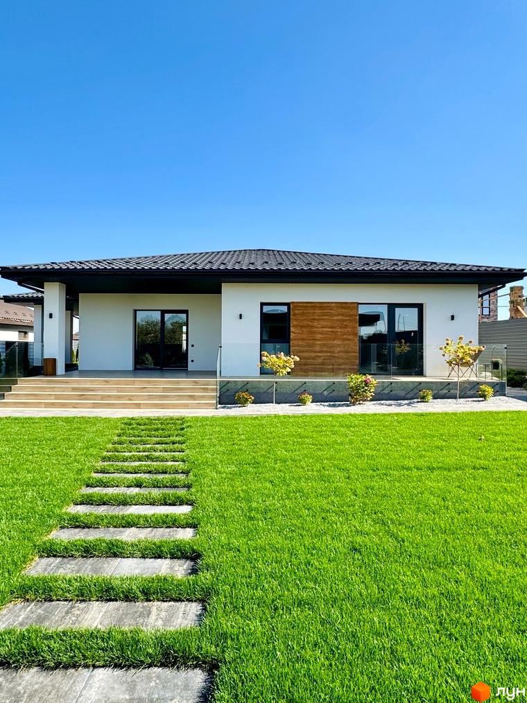 Зображення будинку в Котеджному містечку Bratske Home з великими вікнами та доглянутим газоном. На території облаштовано пішохідну доріжку.