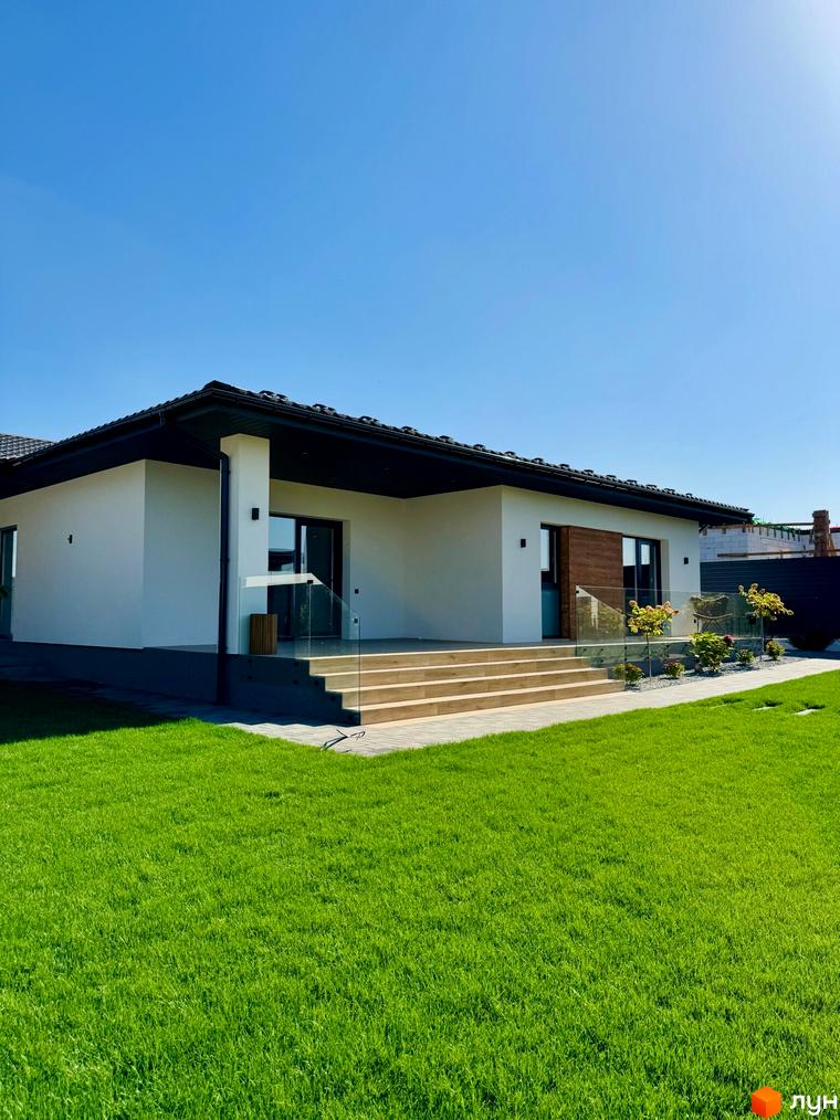 Вигляд будинку в Котеджному містечку Bratske Home з великою зеленою галявиною перед ним. На задньому плані видно частину сусіднього будинку.