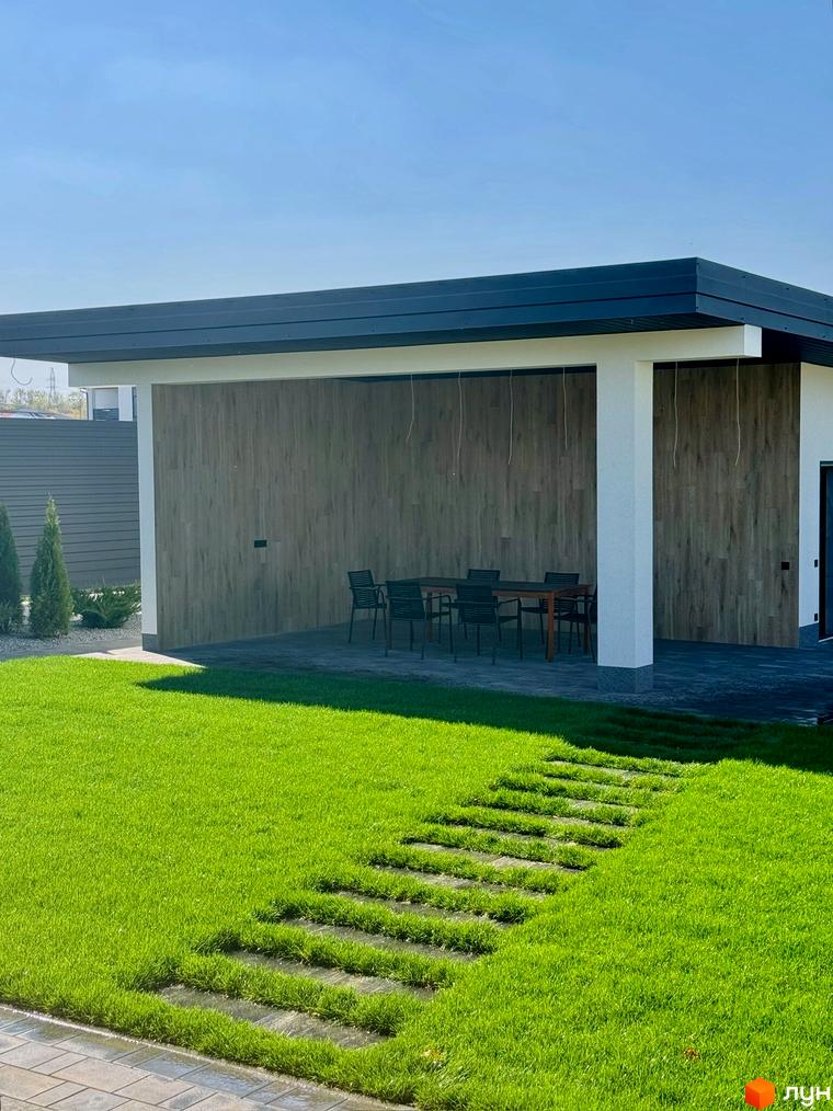 Зображення будинку в Котеджному містечку Bratske Home з терасою та доглянутим газоном. Вигляд на прибудинкову територію.