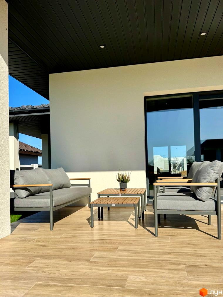 Екстер'єр Котеджного містечка Bratske Home з терасою та плетеними меблями. Вигляд на будинок з великими вікнами та дерев'яним покриттям підлоги.