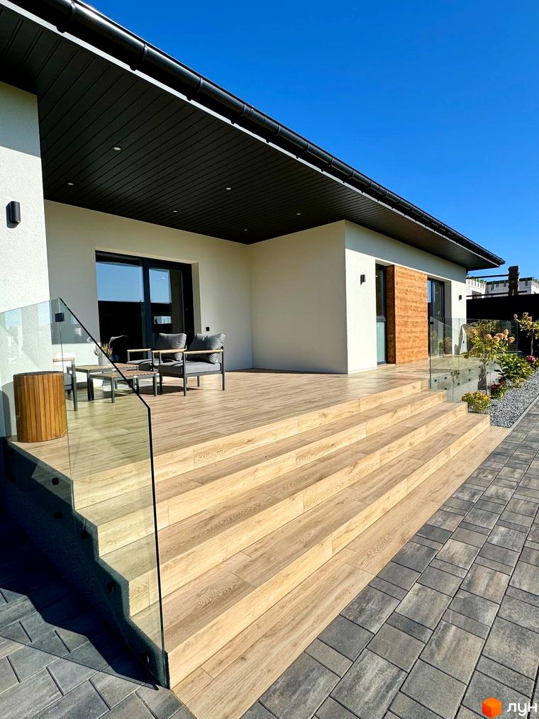 Зовнішній вигляд будинку в Котеджному містечку Bratske Home з терасою та сходами. Навколо будинку облаштована прибудинкова територія.