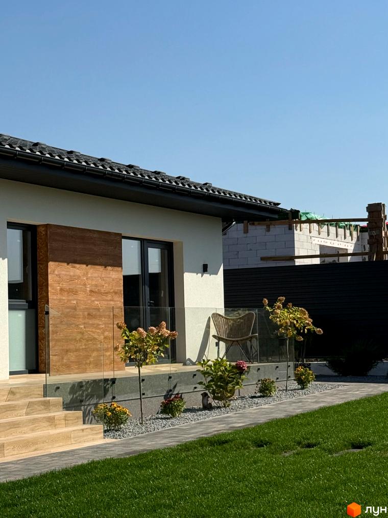 Вигляд будинку в Котеджному містечку Bratske Home з терасою та зеленим газоном. Поруч доріжка з тротуарної плитки.