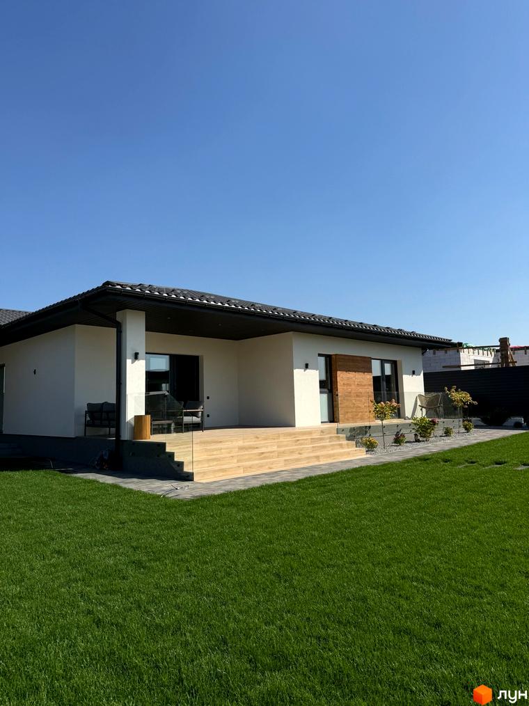 Вигляд будинку в Котеджному містечку Bratske Home з великою терасою та зеленим газоном. На задньому плані видно огорожу.