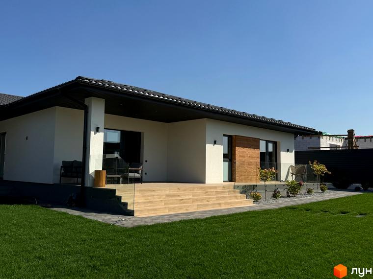 Зображення будинку в Котеджному містечку Bratske Home з терасою та газоном. На задньому плані видно будівництво сусідніх будинків.