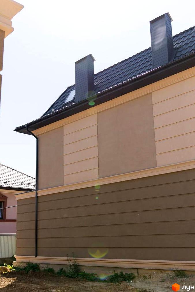 Фасад будинку в Котеджному містечку 5 element з коричневим оздобленням та чорною черепицею на даху. Навколо будинку видно зелену траву.