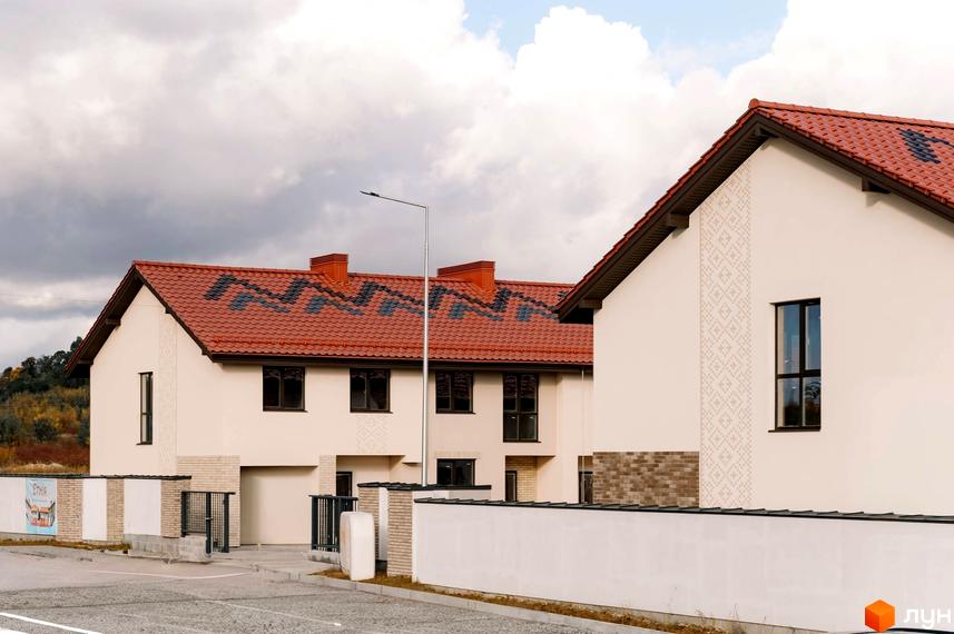 Зовнішній вигляд Котеджного містечка Етнія з червоним дахом та білими стінами. На передньому плані видно огорожу та дорогу.