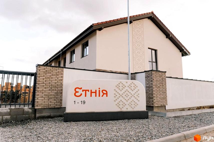 Зовнішній вигляд будинку в Містечку котеджів Етнія з прибудинковою територією. На передньому плані вивіска з назвою комплексу.