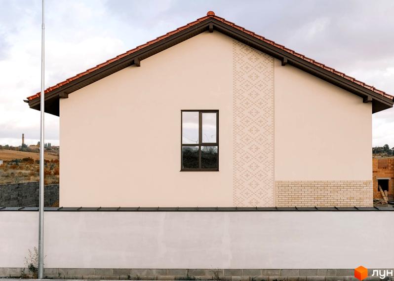 Зовнішній вигляд будинку в Котеджному містечку Етнія з вікном та декоративною вставкою. Видно частину прибудинкової території.