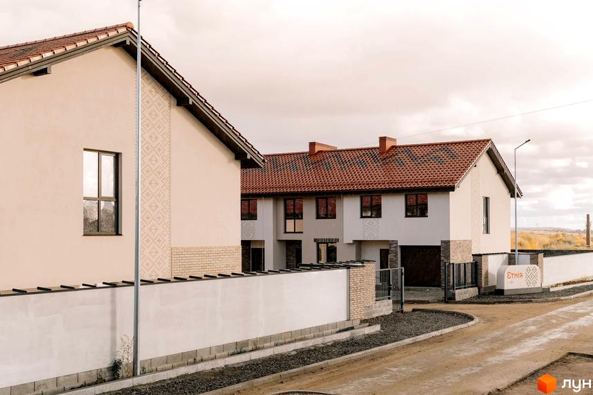 Зображення фасаду та прибудинкової території котеджної забудови Етнія. Вигляд на таунхауси з червоною черепицею та білими стінами.