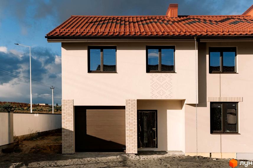 Зовнішній вигляд двоповерхового будинку в Котеджному містечку Етнія з червоною черепицею та гаражем. Навколо будинку піщаний ґрунт.