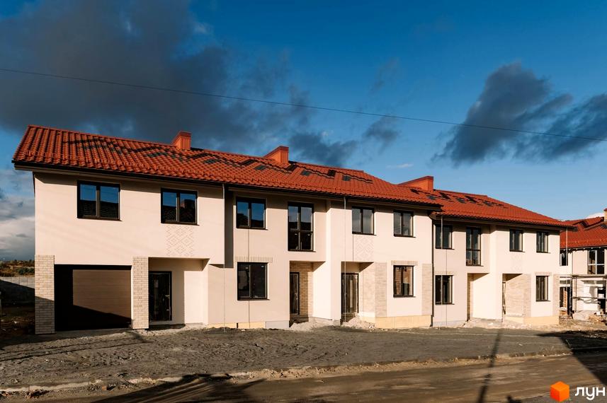 Зображення Котеджного містечка Етнія з фасадом будинку з червоним дахом та вікнами. Навколо будинку видно піщану землю.