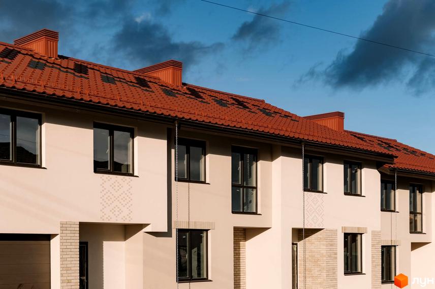 Зовнішній вигляд будинку в Котеджному містечку Етнія з червоним дахом та великими вікнами. На тлі блакитне небо з хмарами.