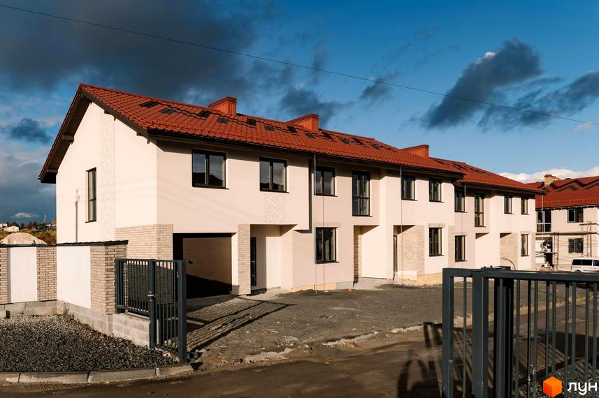 Зовнішній вигляд котеджного містечка Етнія з червоними дахами та світлими стінами. Подвір'я з бруківкою та металевими огорожами.