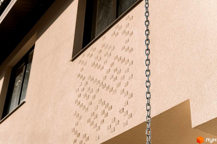 Фасад будинку в Котеджному містечку Етнія з вікнами та декоративним оздобленням. На передньому плані металевий ланцюг.
