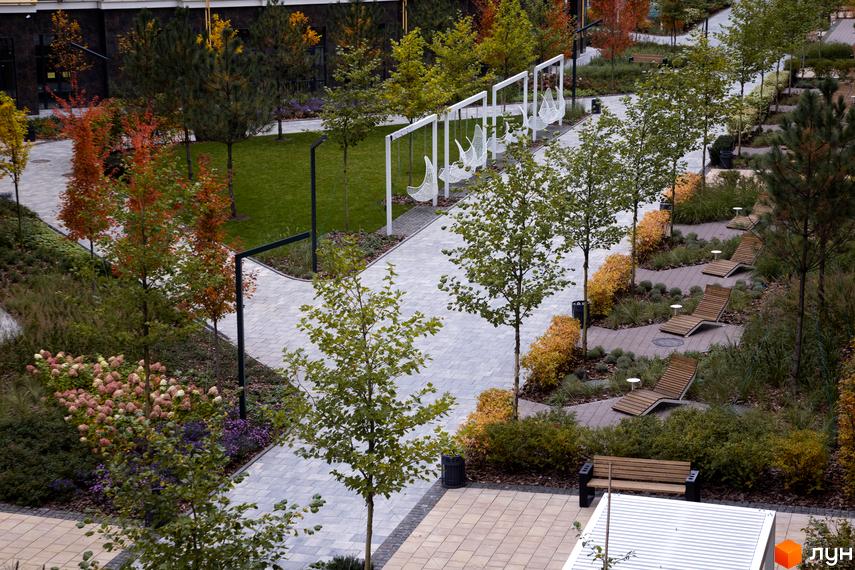 Вигляд зверху на Житловий район Синергія Сіті з пішохідними алеями, лавками та підвісними гойдалками. Озеленена територія з деревами та кущами.