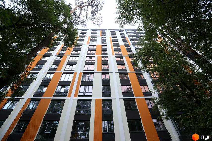 Зображення фасаду Житлового комплексу Favorit Premium з вікнами та балконами. Вид на багатоповерховий будинок з прилеглими деревами.