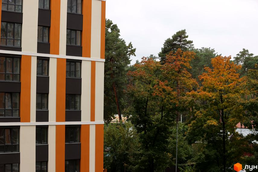 Зображення фасаду Житлового комплексу Фаворит Premium з вікнами та помаранчевими вставками. На задньому плані дерева з жовтим листям.