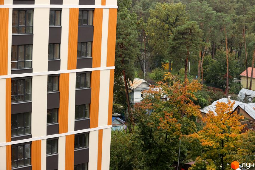 Фасад Житлового комплексу Фаворит Premium з вікнами та смугастим оздобленням. Навколо будинку дерева з помаранчевим листям та інші будівлі.