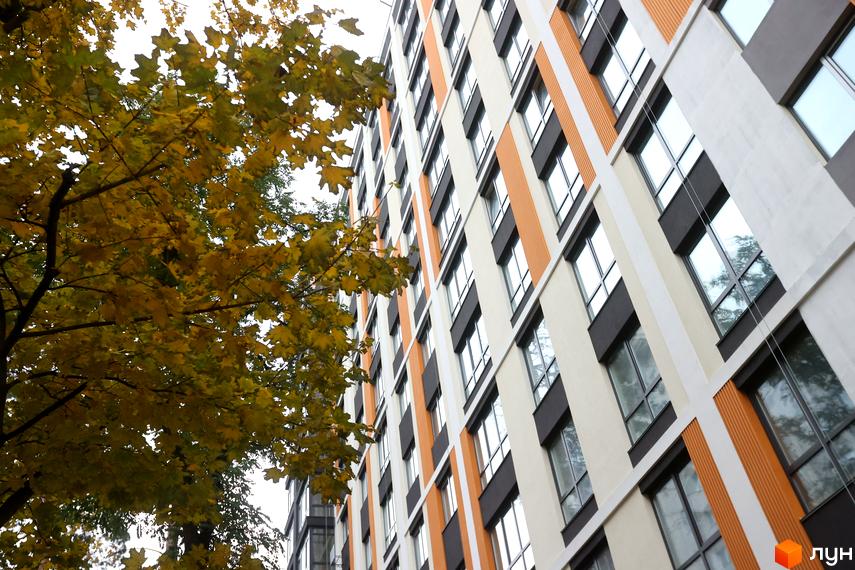 Зображення фасаду Житлового комплексу Фаворит Premium з великими вікнами та яскравими вставками. Поруч розташовані дерева з жовтим листям.