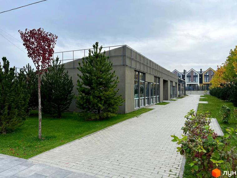 Зображення фасаду будівлі Житлового комплексу Sanville Park з великими вікнами. Навколо зелена територія з деревами та доріжкою з тротуарної плитки.