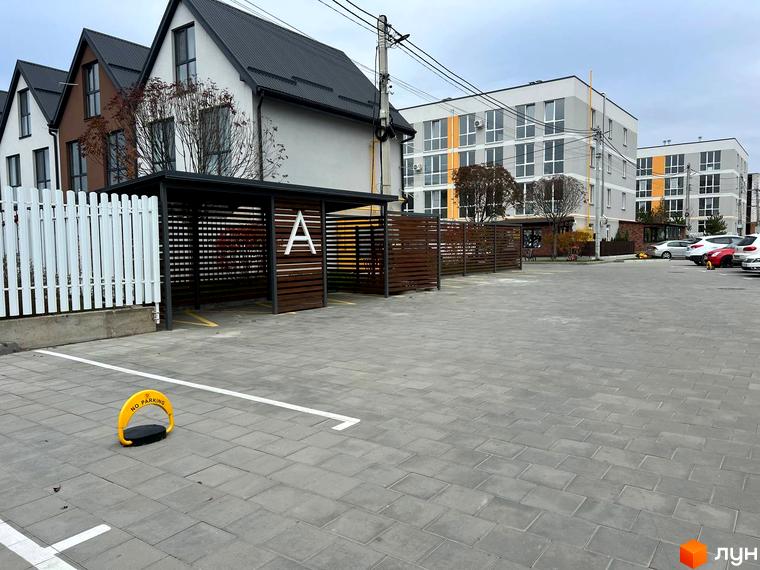 Вигляд на Житловий комплекс Sanville Park з парковкою та будинками. На передньому плані розміщена перешкода для паркування.
