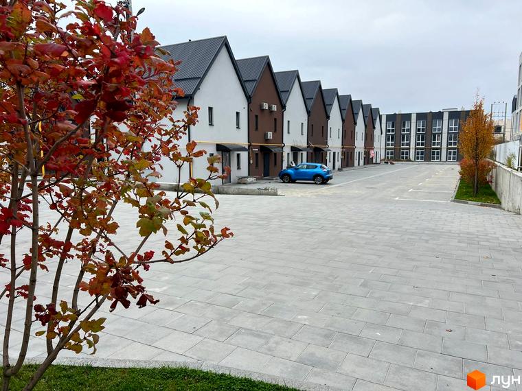 Вигляд на таунхауси в Житловому районі Sanville Park з парковкою та деревами з червоним листям на передньому плані.