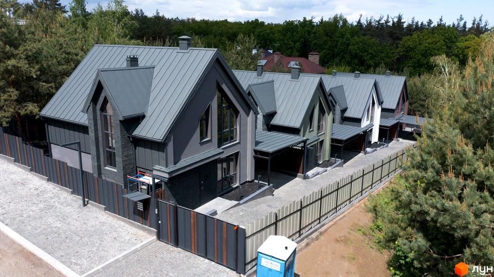 Зображення котеджів у Котеджному містечку Strilets'sky з сірими дахами та темними фасадами. Навколо будинків зелені дерева та огорожа.