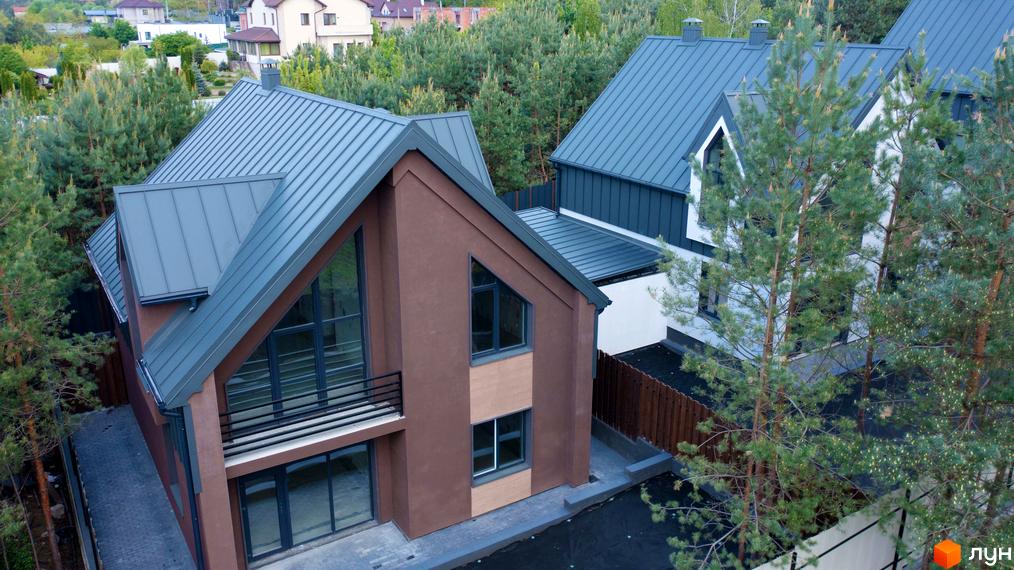 Зображення будинку в Котеджному містечку Strilets'sky з великими вікнами та сірим дахом. Навколо будинку зелені дерева.