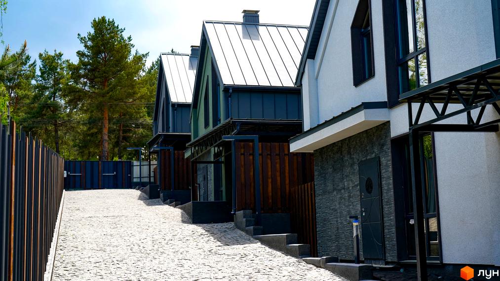 Зображення будинків Котеджного містечка Strilets'sky з металевими дахами та дерев'яними елементами. Подвір'я викладене бруківкою.