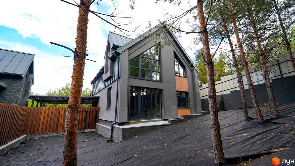 Вигляд будинку в Котеджному містечку Strilets'sky з великими вікнами та сірим фасадом. Навколо будинку дерева та чорна тканина на землі.