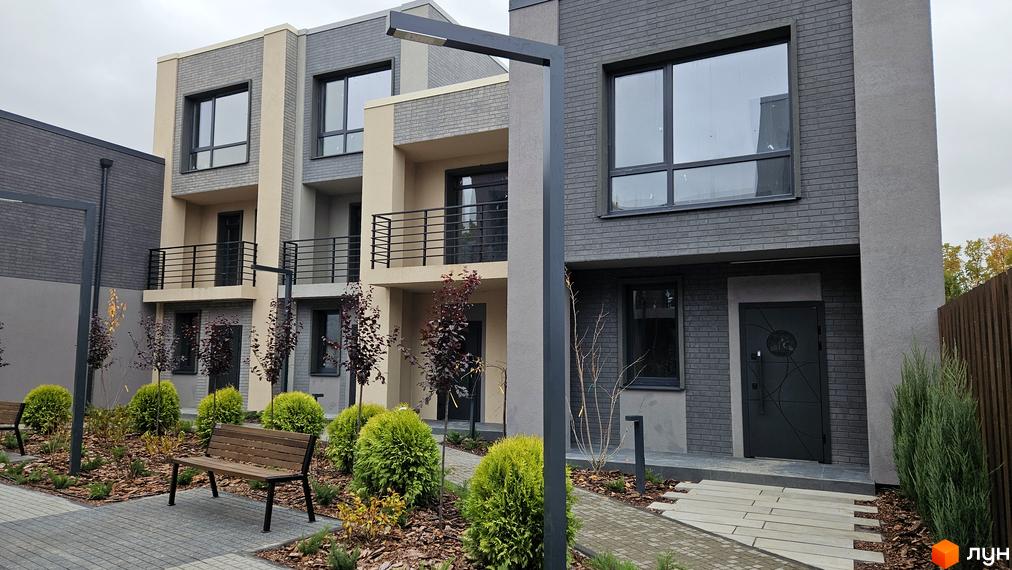Зовнішній вигляд таунхаусів Sвій Dім 2 з сірого та бежевого цегли, з великими вікнами та балконами. Навколо будинку зелені насадження та лавки.