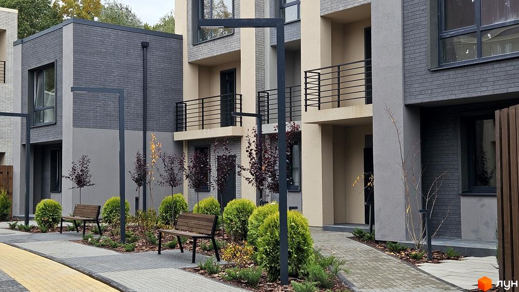 Зображення таунхаусів Sвій Dім 2 з сірого цегли, з балконами та лавками на прибудинковій території.