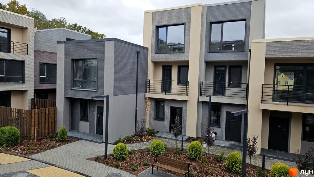 Зображення таунхаусів Sвій Dім 2. Триповерхові будинки з сірим цегляним фасадом та великими вікнами, перед будинками висаджені кущі.