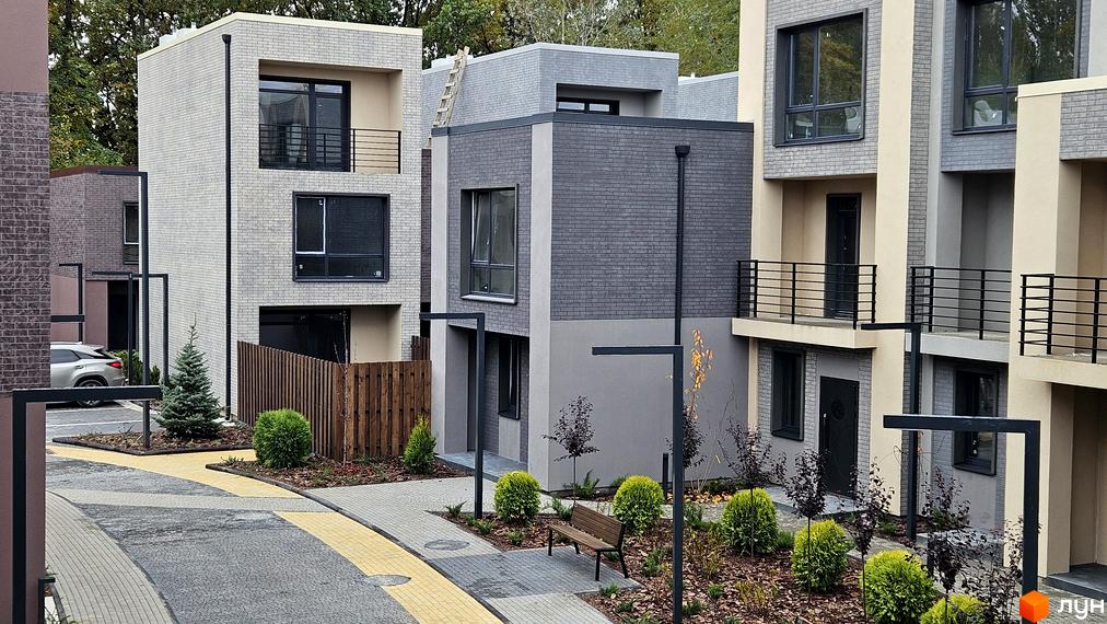 Зображення таунхаусів Sвій Dім 2. Двоповерхові будинки з сірого та бежевого цегли, з балконами та великими вікнами, розташовані серед зелених насаджень.