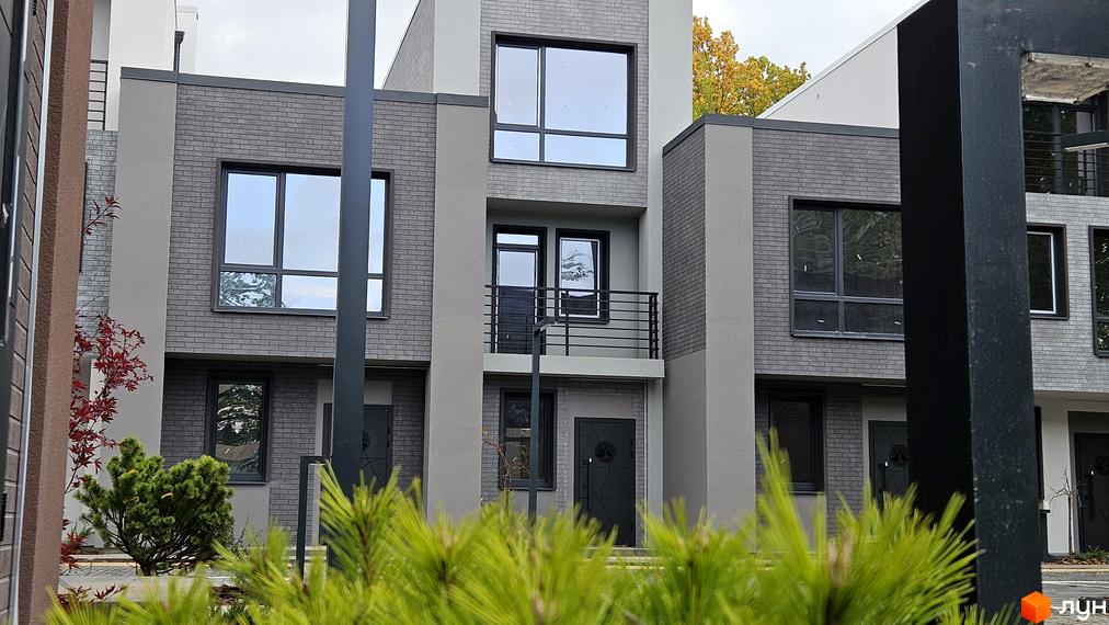 Зовнішній вигляд таунхаусів Sвій Dім 2 з сірого цегли, з великими вікнами та озелененням навколо. Вигляд фасаду таунхаусів.