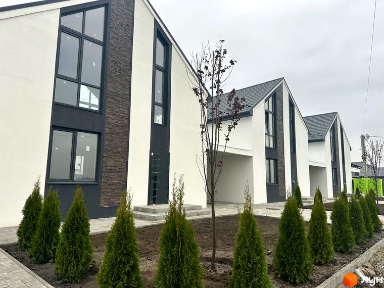 Вигляд будинків у Котеджному містечку DESNA HOMES з великими вікнами та обробкою під камінь. Навколо висаджені туї та дерева.