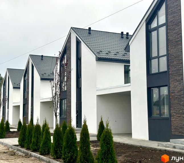 Зображення Котеджного містечка DESNA HOMES: ряд нових будинків з сірими дахами та білими стінами. Перед будинками висаджені зелені туї.