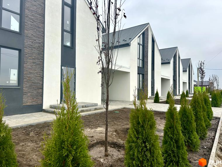 Зовнішній вигляд котеджного містечка DESNA HOMES: двоповерхові будинки з білими стінами та темними вікнами. На території висаджені туї та дерева.
