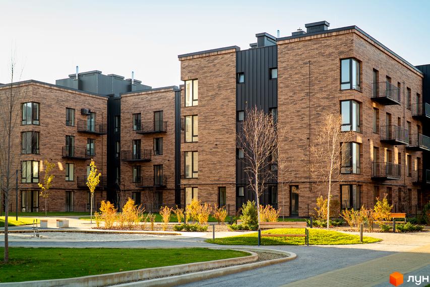 Зображення фасаду та прибудинкової території Житлового комплексу Долішній. На фото видно будівлю з цегли та зелені насадження.