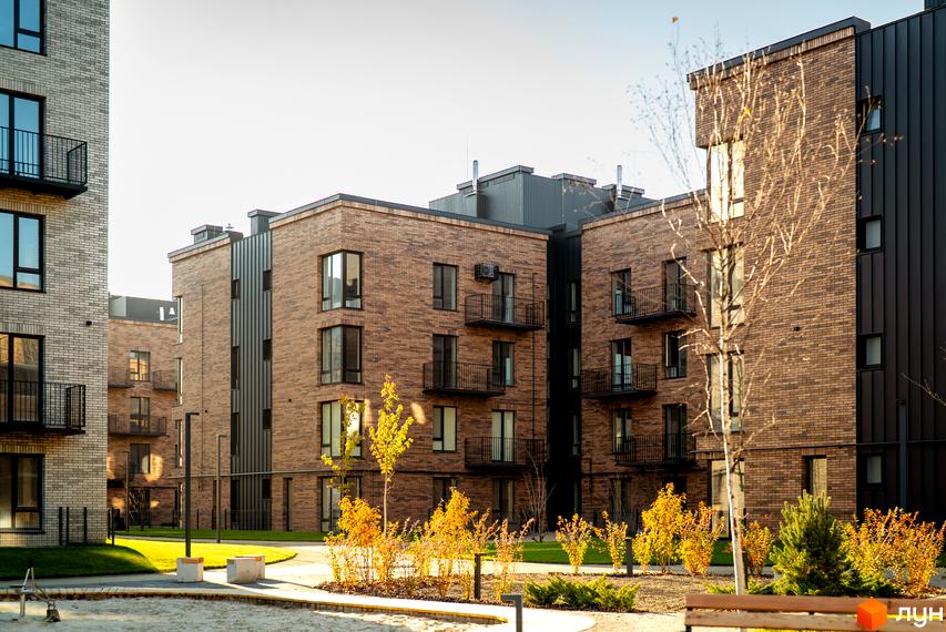 Зображення фасаду та прибудинкової території Житлового комплексу Долішній. На фото видно цегляні будинки та зелені насадження.