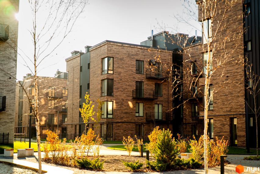 Зображення фасаду та прибудинкової території Житлового комплексу Долішній. Будинки з цегли, поруч зелені насадження.