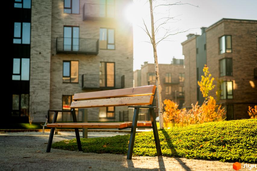 Вигляд будинку в Житловому комплексі Долішній. На передньому плані лавка, навколо зелені насадження та дерева.