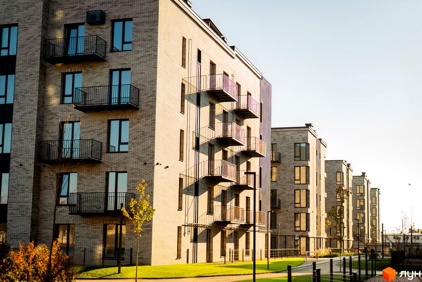 Зображення фасаду Житлового комплексу Долішній з балконами. Вигляд на прибудинкову територію з газоном та пішохідною доріжкою.