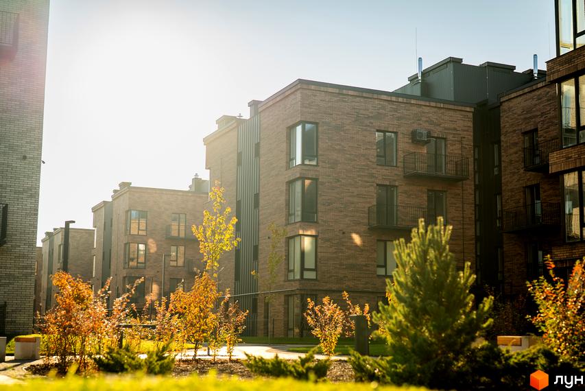 Вигляд фасаду та прибудинкової території Новобудови Долішній. Цегляні будинки з великими вікнами та балконами, зелені насадження.