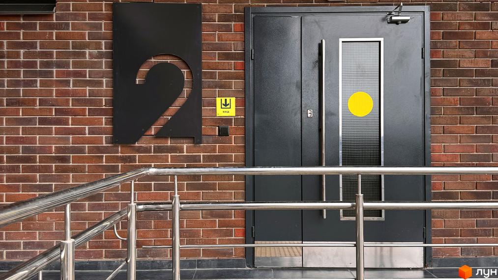 Фасад житлового комплексу Стандарт з номером 2 біля входу. Цегляна будівля з металевими поручнями.