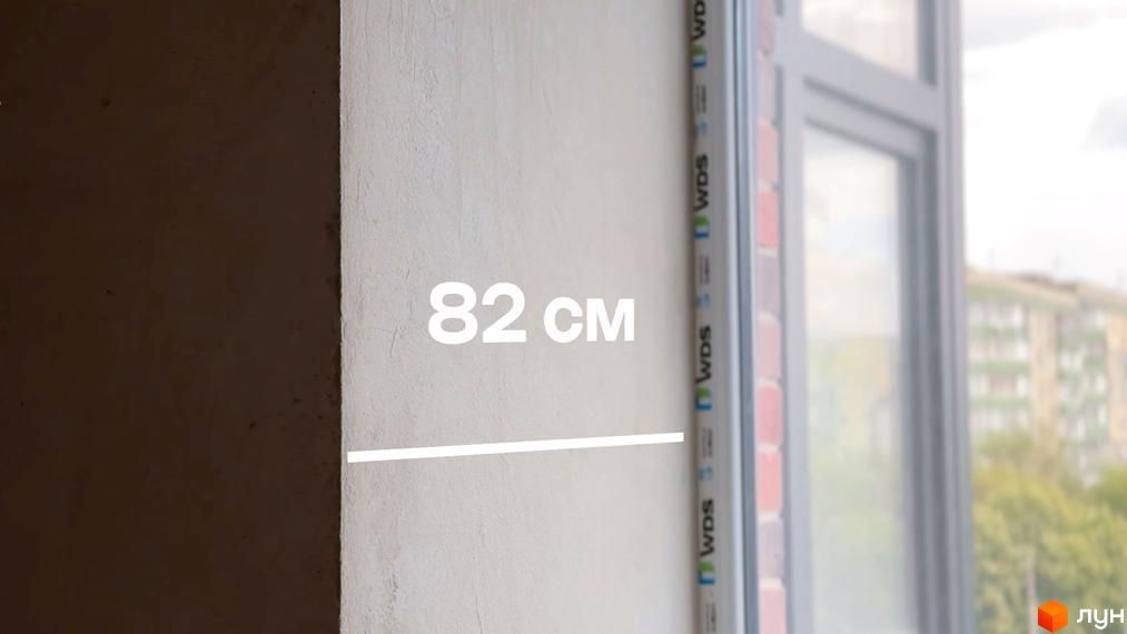 Фото стіни з розмірами в квартирі у Будівельному проєкті Стандарт. Вигляд з вікна на будівлі та зелені насадження.