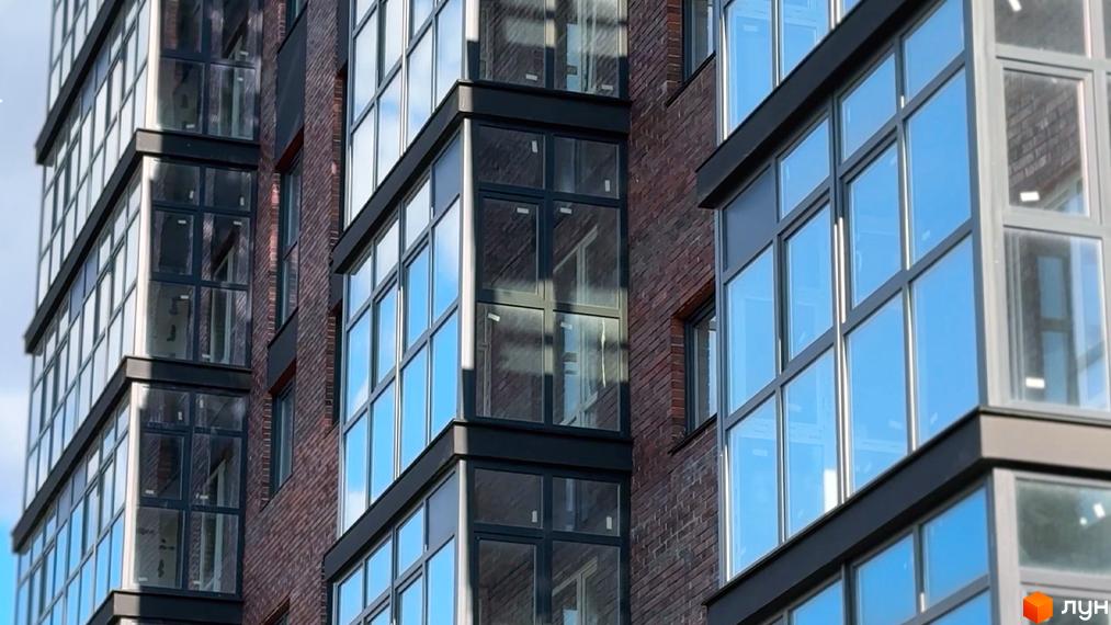 Зображення фасаду Житлового комплексу Стандарт з великими вікнами та цегляним оздобленням. На фото видно частину будівлі та скління балконів.