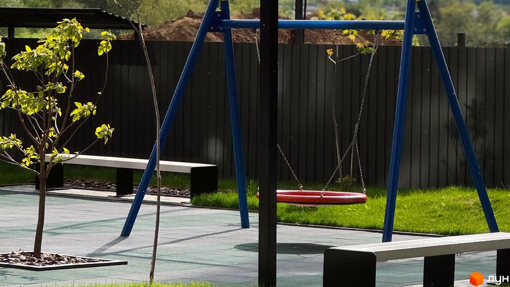 Зображення дитячого майданчика з гойдалкою та лавками на території Житлового комплексу Стандарт.