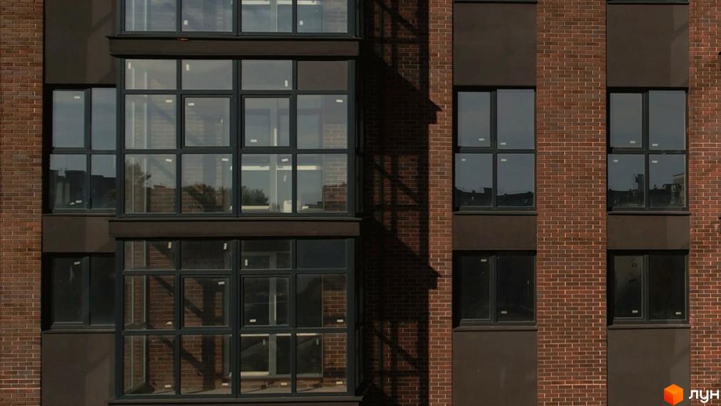 Фасад будинку з великими вікнами в Житловому комплексі Стандарт. Цегляна кладка та темні віконні рами.